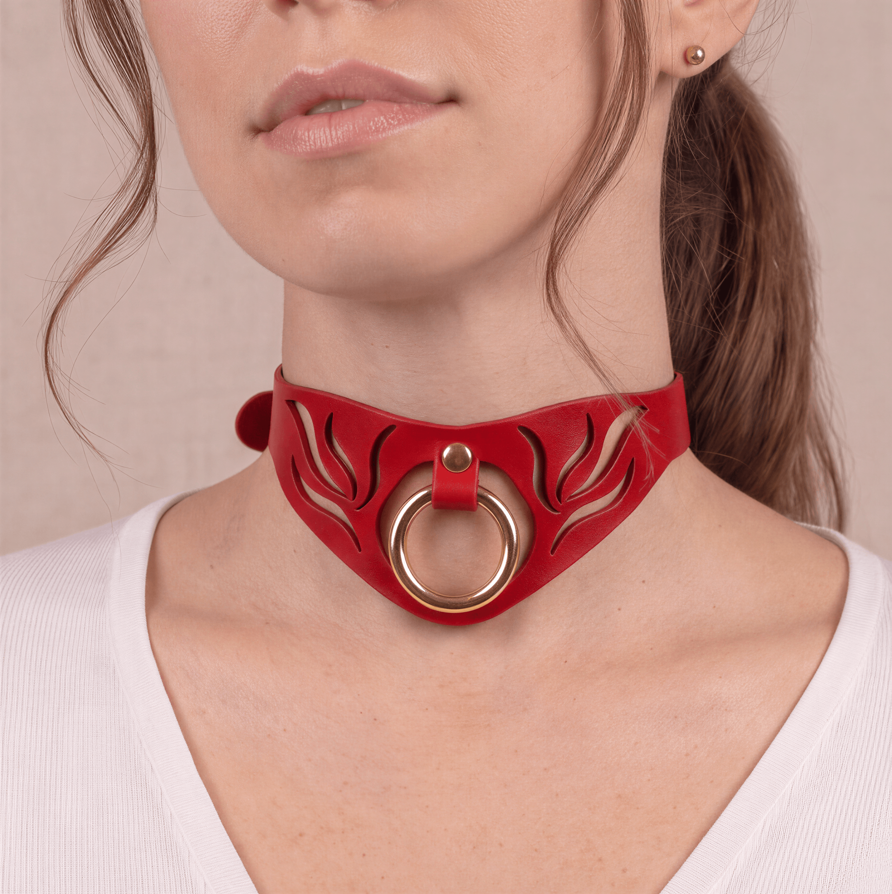 A close-up of a woman's neck and chin wearing a red choker necklace with a gold ring.