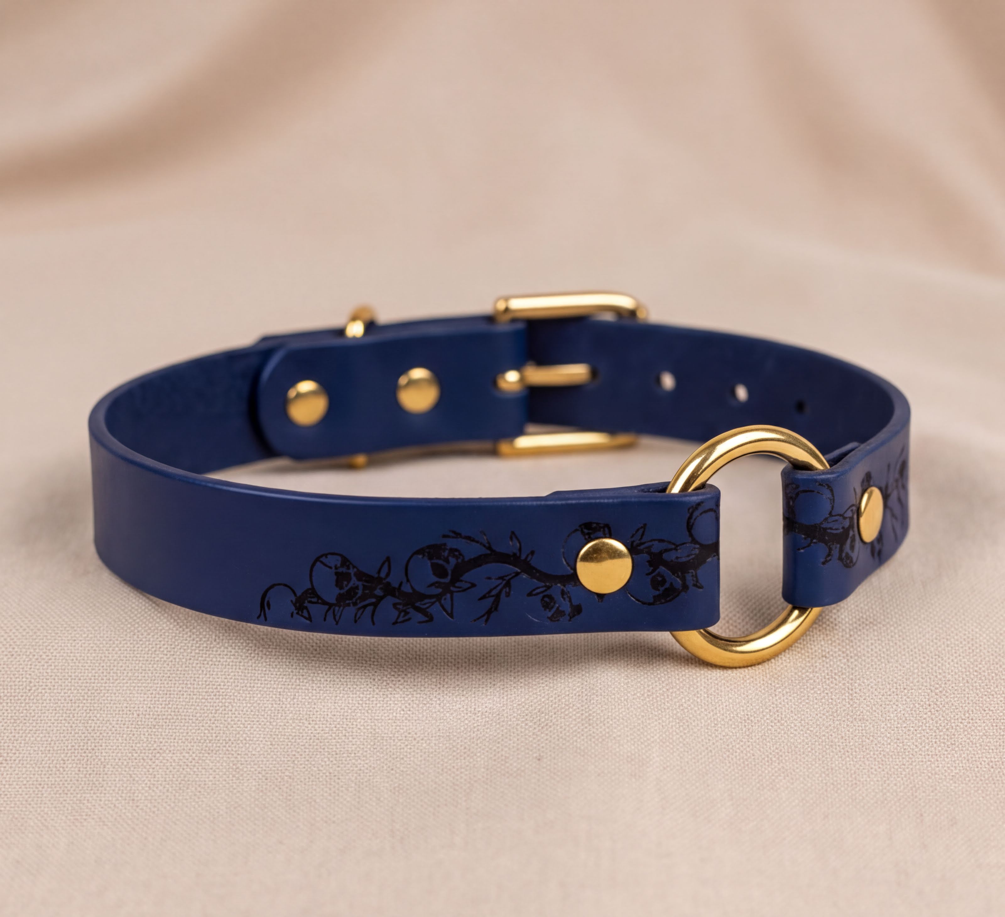 A blue leather collar with a gold-colored buckle and a floral design on the strap.