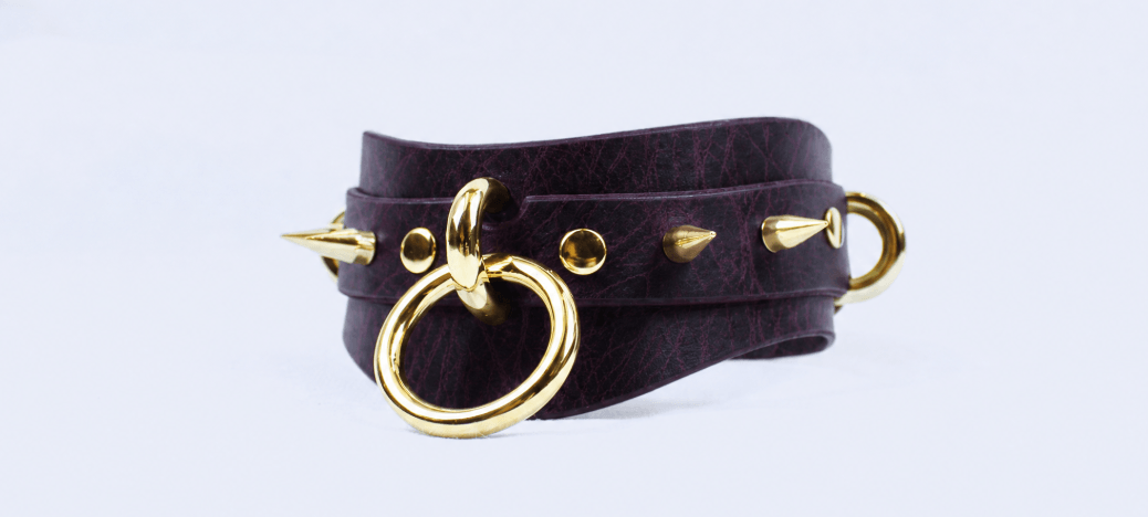 A purple leather choker necklace with gold studs and a gold ring.