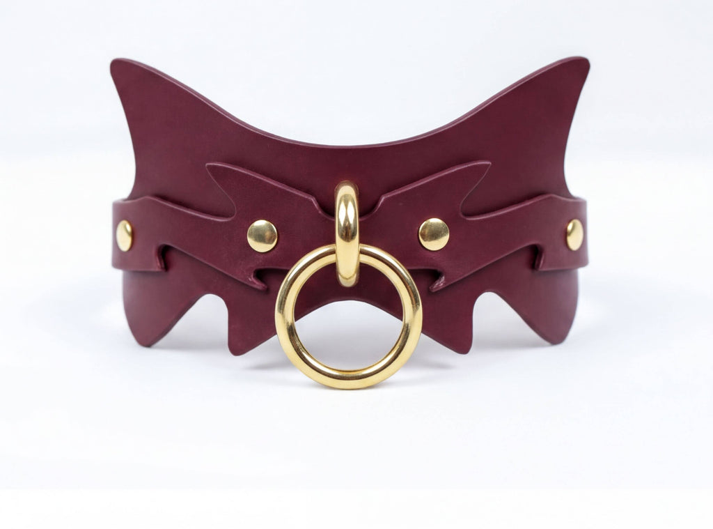 A burgundy leather choker necklace with a gold-colored metal ring and a decorative design on the front.