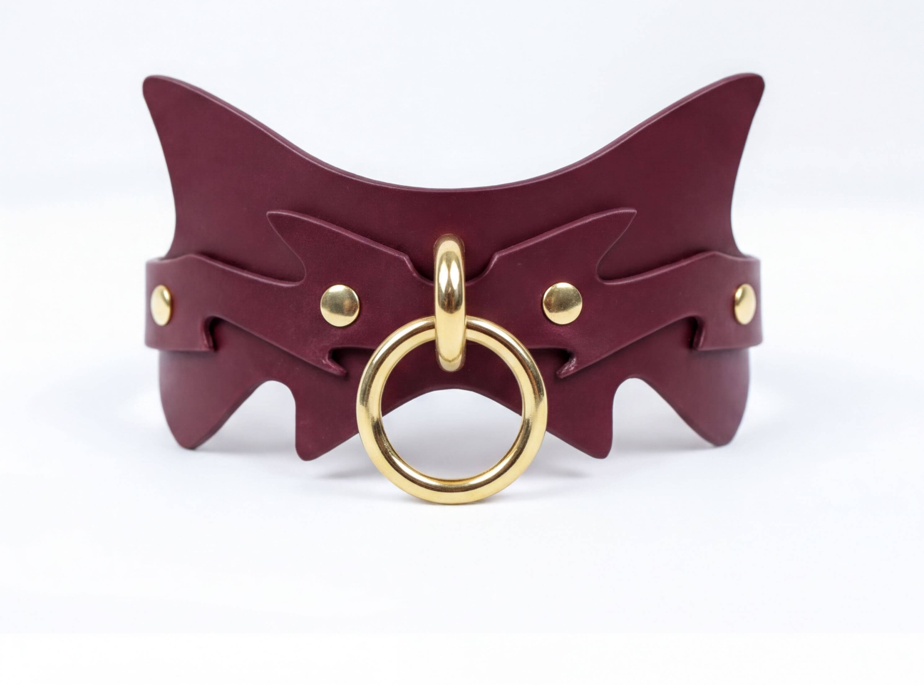 A burgundy leather choker necklace with a gold-colored metal ring and a decorative design on the front.