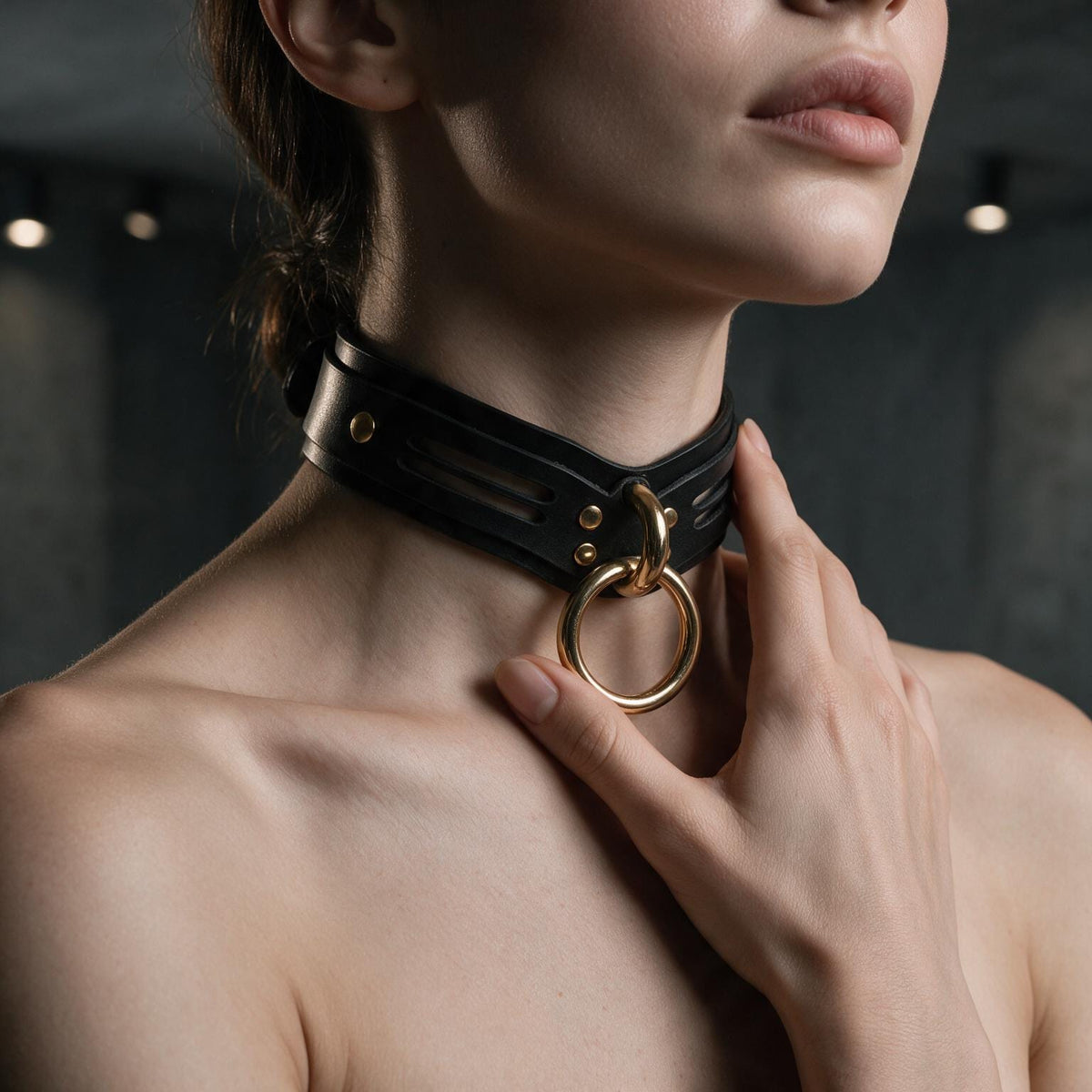 A close-up of a woman's neck and chest wearing a black leather choker necklace with a gold ring.