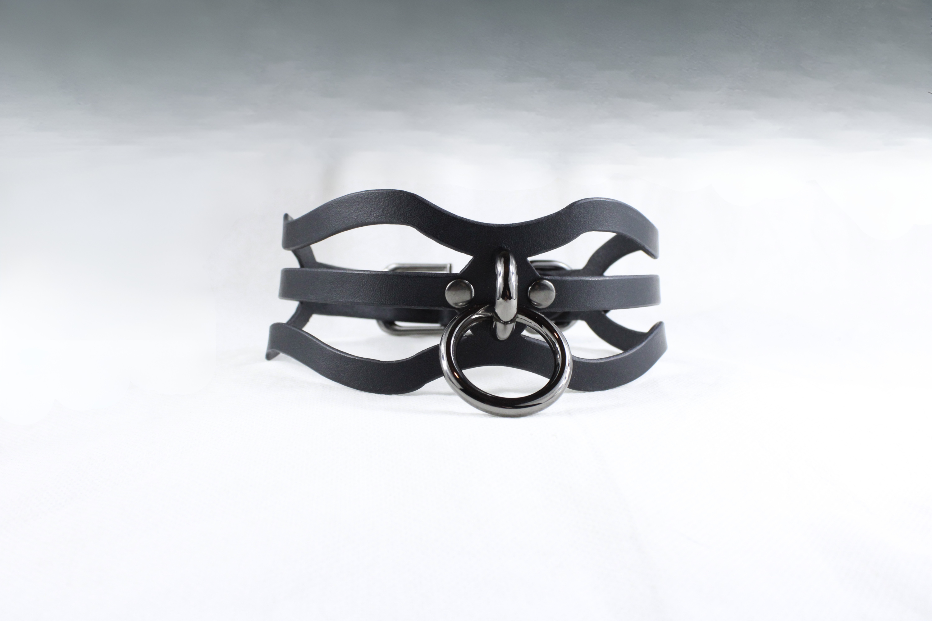 A black leather choker necklace with a metal ring and a curved metal piece.