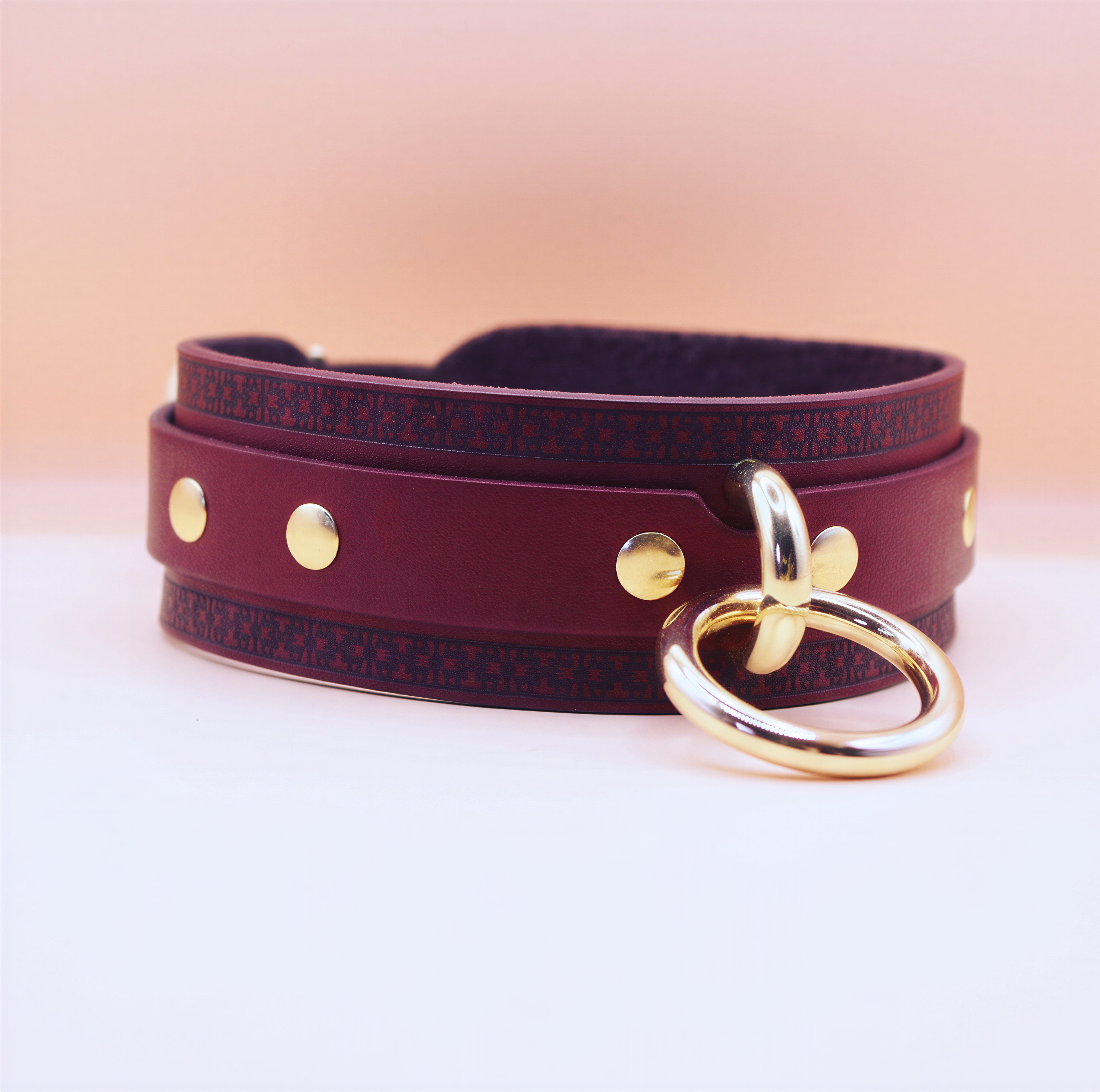 A burgundy leather choker necklace with a gold ring and three gold studs on the front.