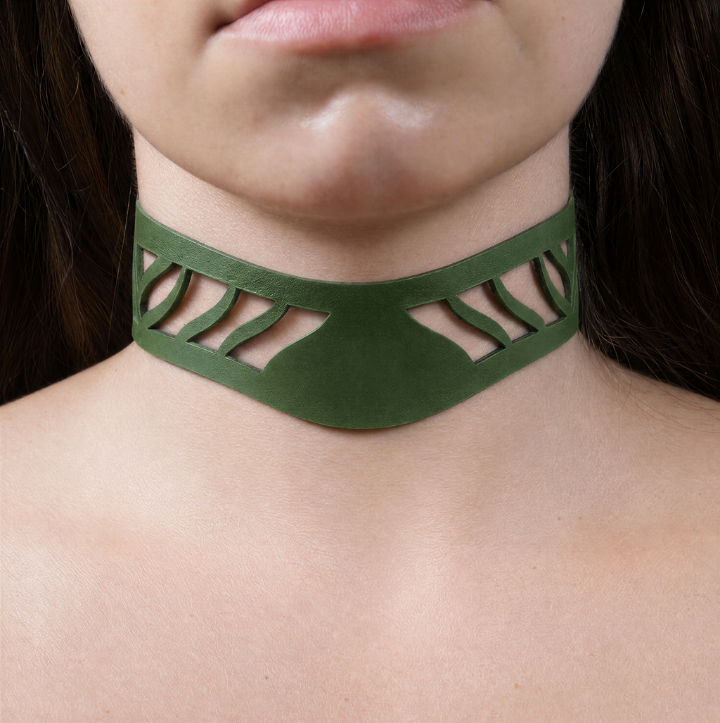 A close-up of a person's neck and chest area wearing a green choker necklace with a unique cutout design.