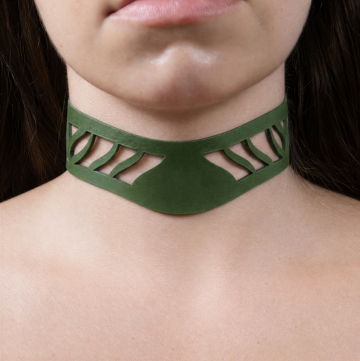 A close-up of a person's neck and chest area wearing a green choker necklace with a unique cutout design.