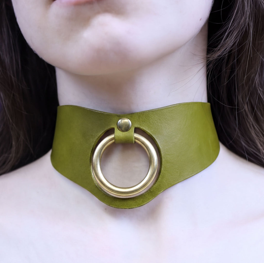 A close-up of a person's neck wearing a green leather choker necklace with a gold ring.