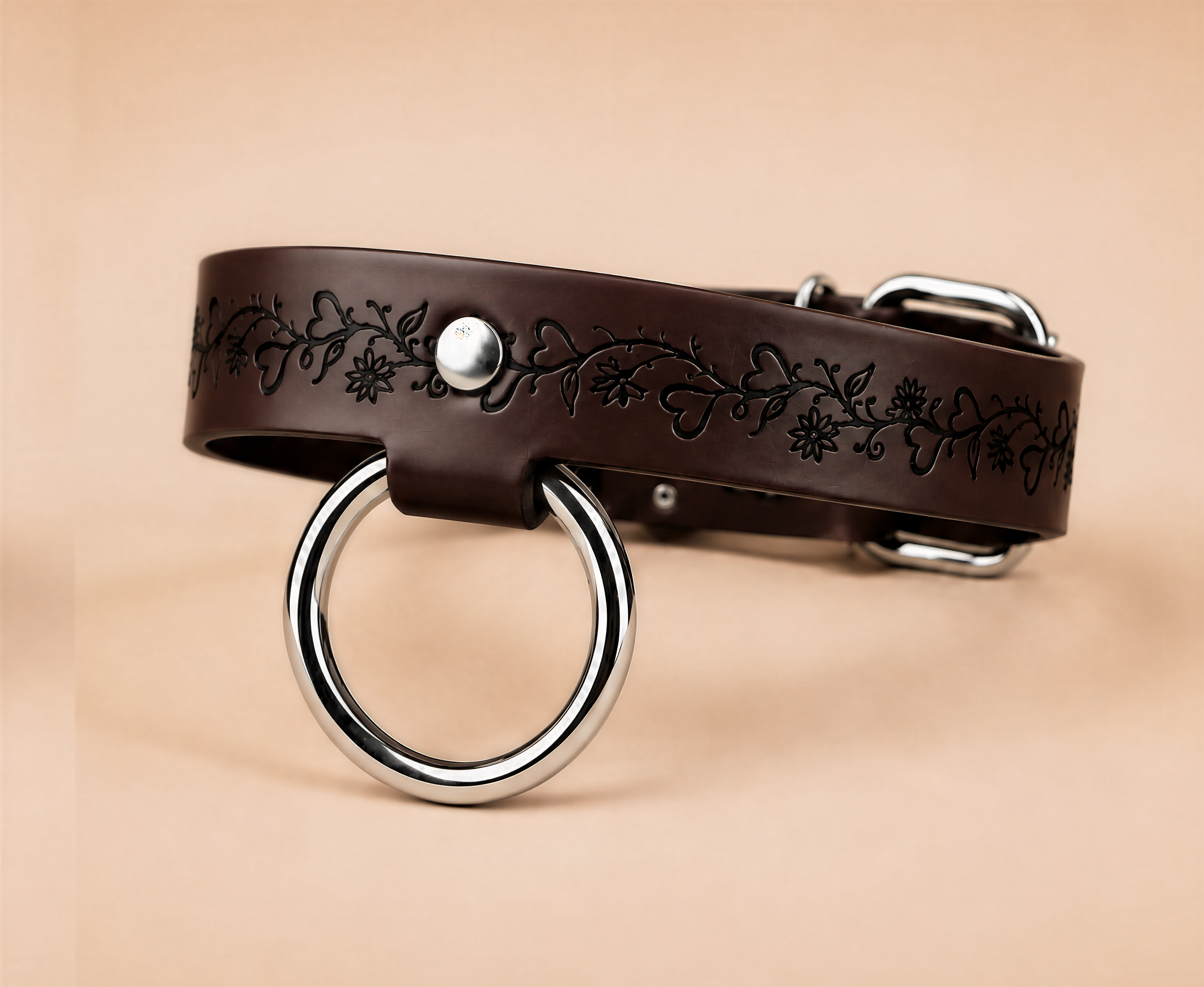 A brown leather collar with a metal ring and a decorative floral pattern on the strap.