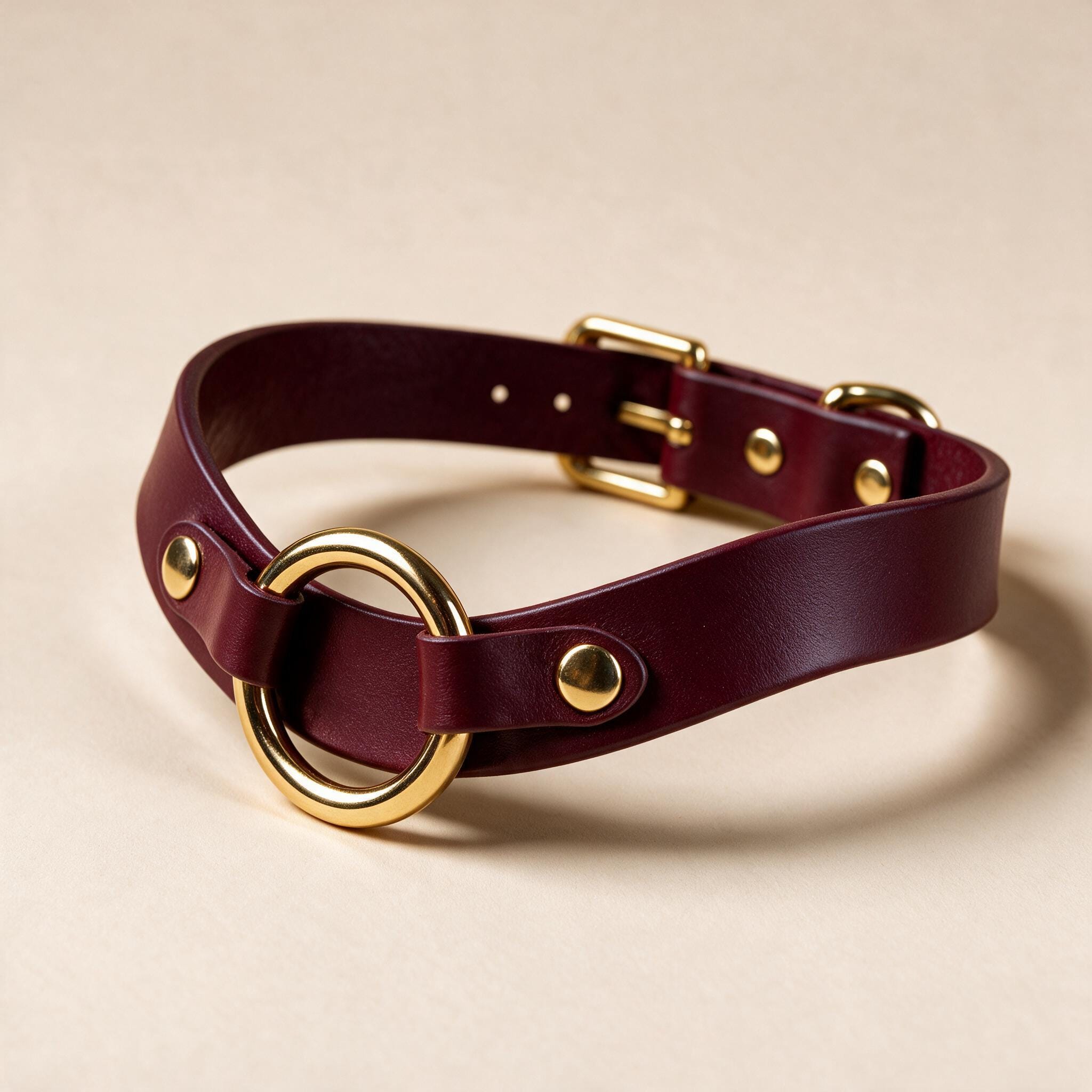 A burgundy leather choker collar with a gold-colored buckle and two gold-colored holes on the front.