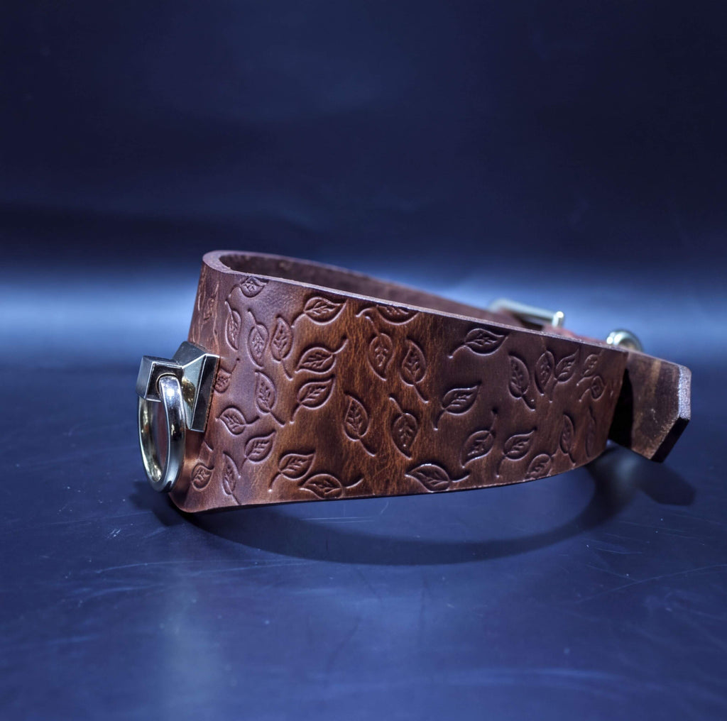 A brown leather belt with a leaf pattern embossed on it, resting on a dark blue surface.