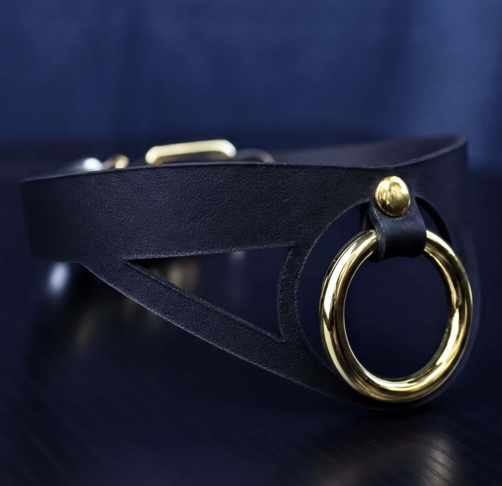 A close-up view of a black leather choker necklace with a gold-colored circular clasp.