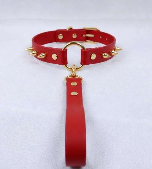 A red, spiked collar with gold studs and a gold-colored loop is displayed against a white background.