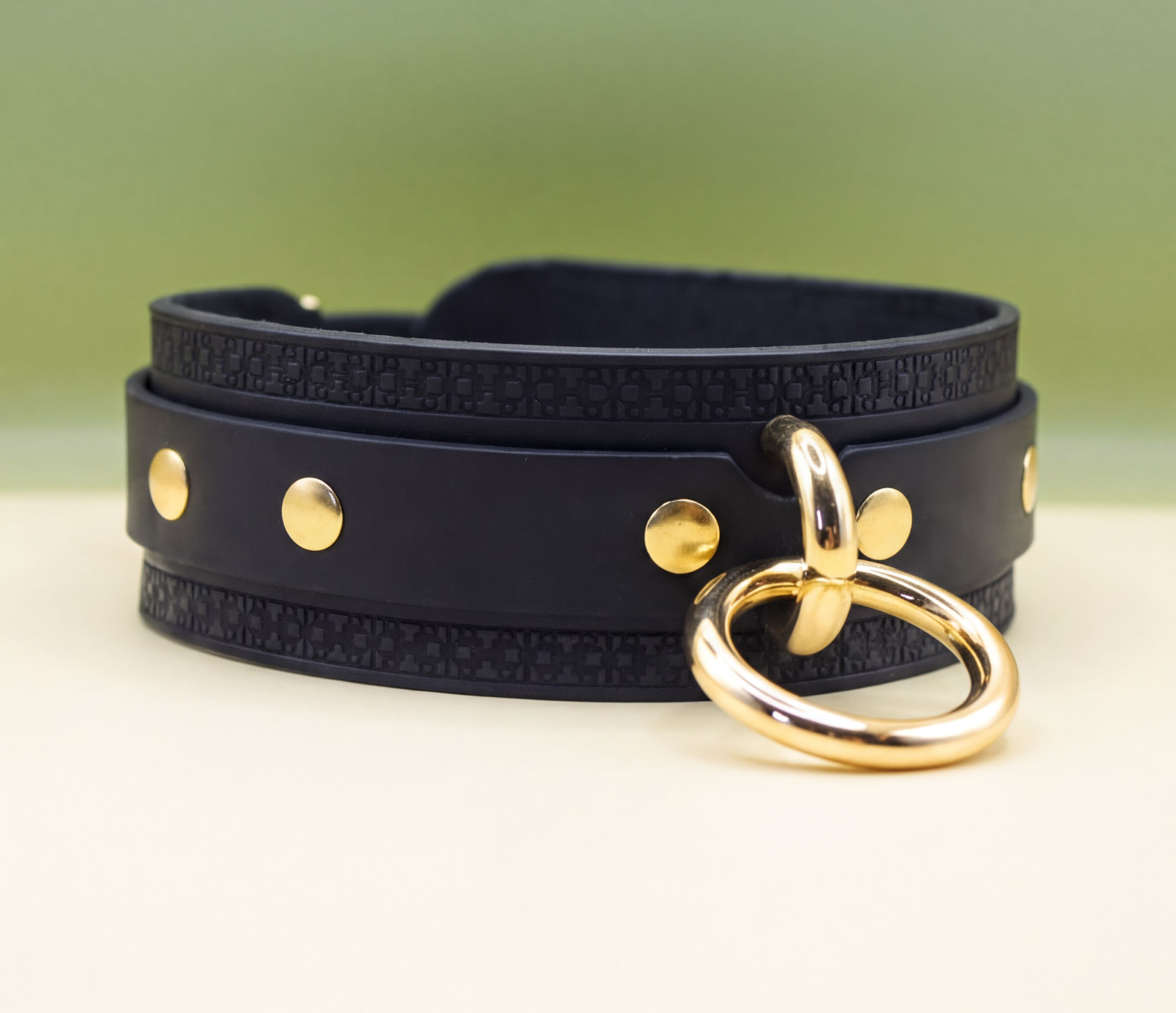 A black leather choker necklace with gold-colored metal studs and a gold-colored metal ring.