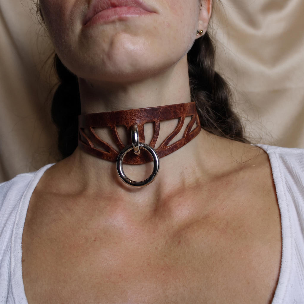 A close-up of a woman's neck and chest area, featuring a leather choker necklace with a metal ring.
