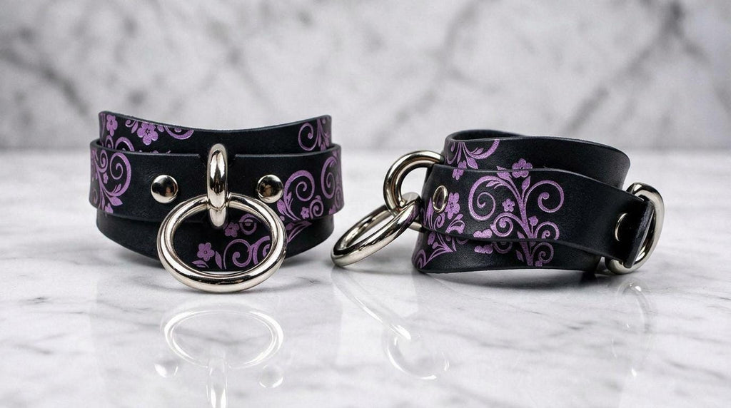 a pair of black leather choker necklaces with purple floral designs and metal rings on the front.