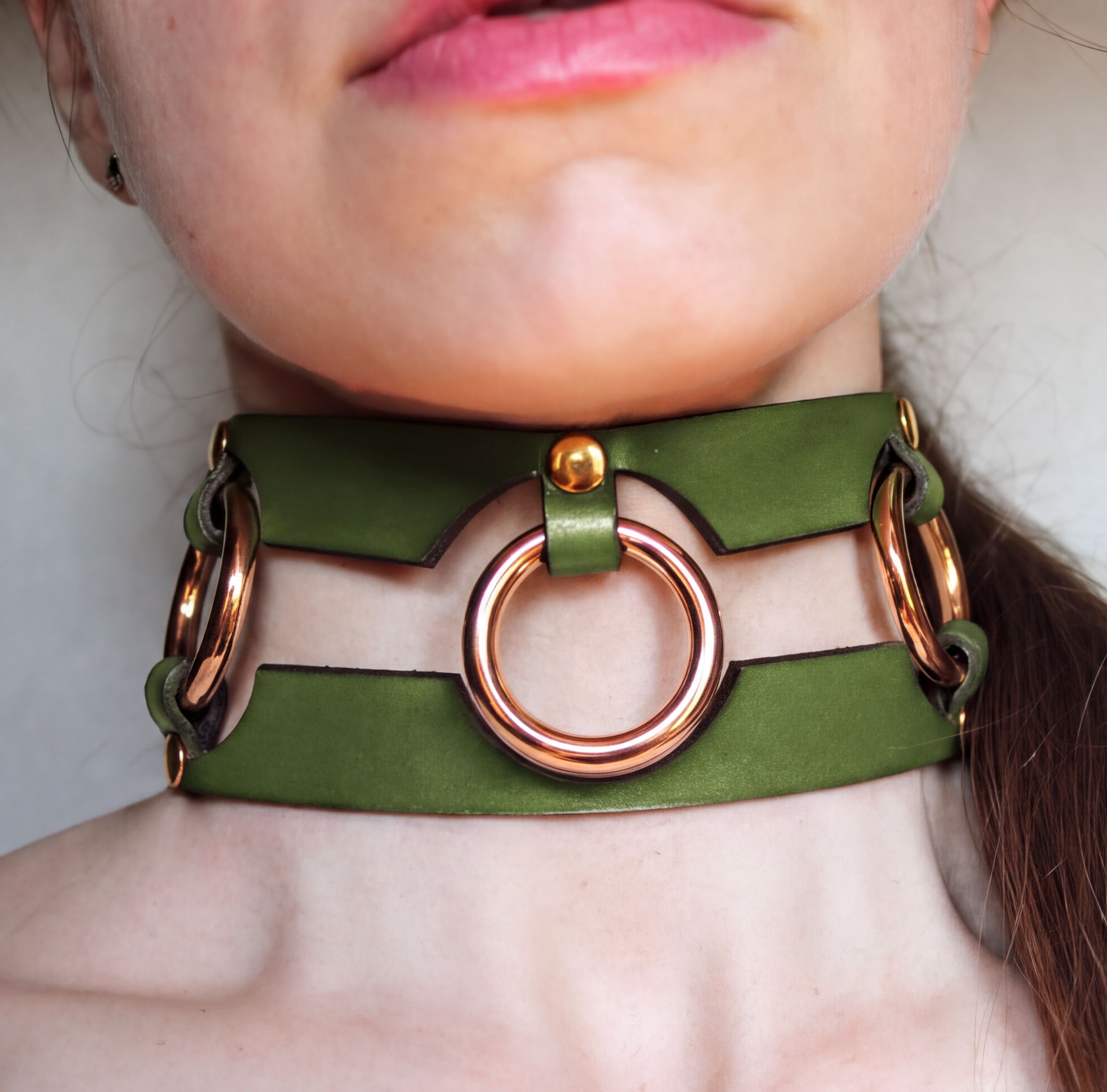 A close-up of a person's neck wearing a green leather choker necklace with gold-colored rings.