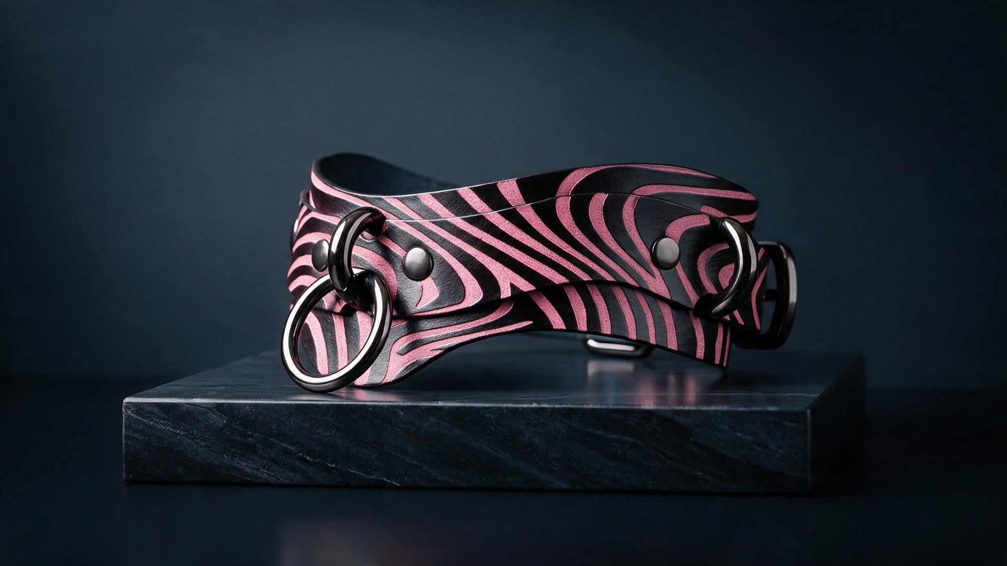 A zebra-striped leather collar with metal rings and buckles is displayed on a black surface against a dark background.
