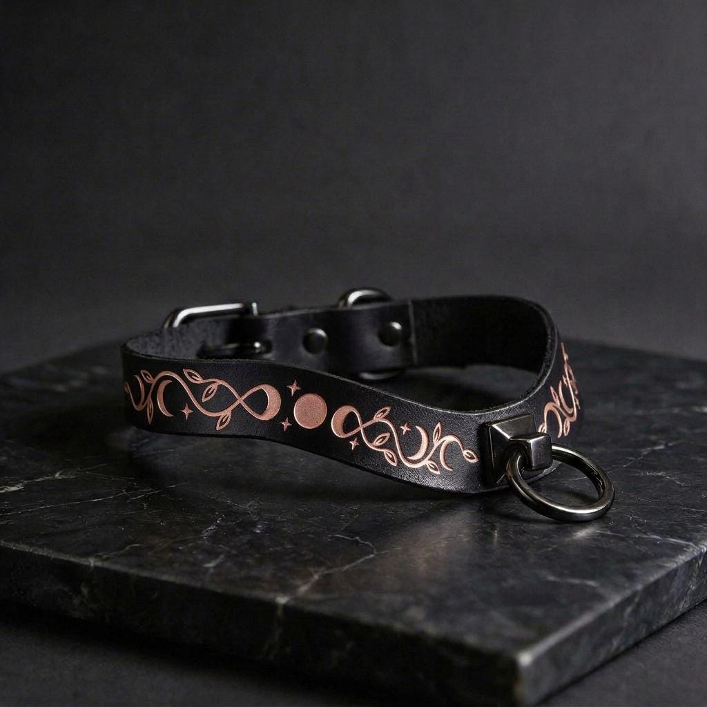 A black leather collar with a metallic, decorative design on it, resting on a dark surface.