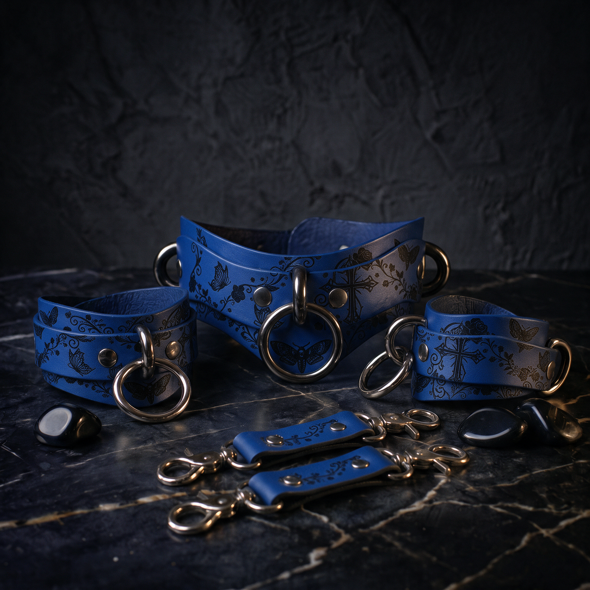 A set of blue leather straps with metal rings and buckles, arranged on a dark surface.