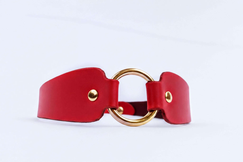 A red leather choker necklace with a gold-colored circular clasp.