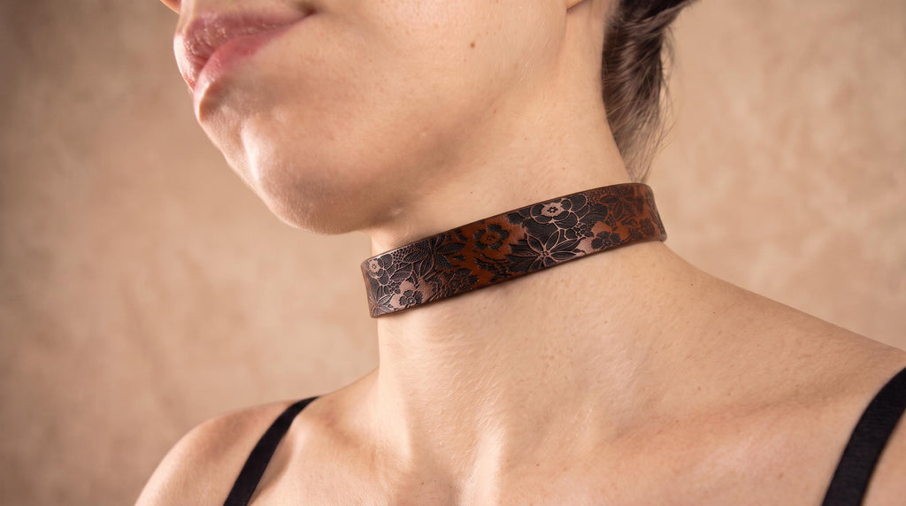 A close-up of a woman's neck and chest area wearing a brown choker necklace with a floral pattern.