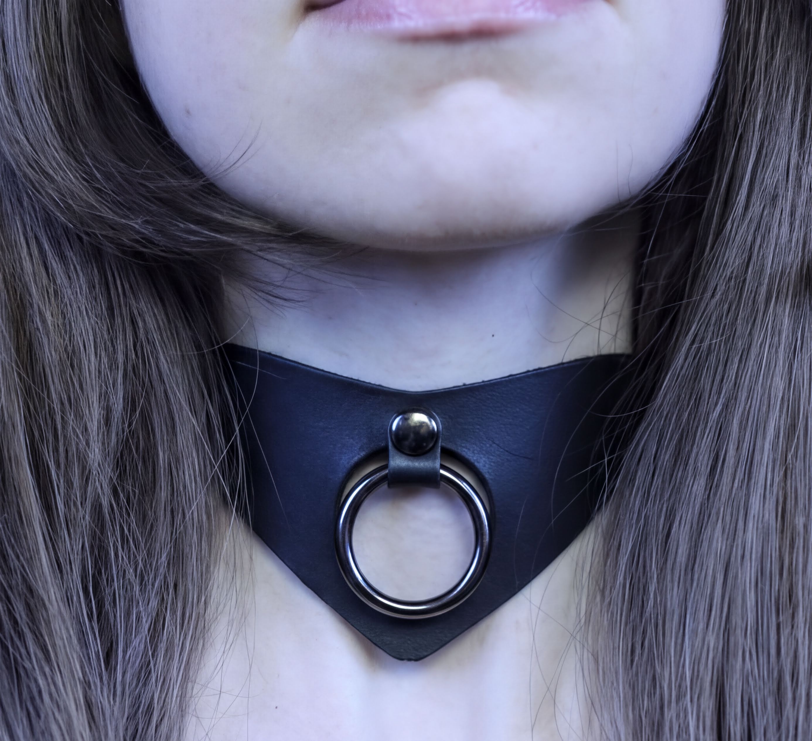 A close-up of a person's neck and chin area, featuring a black leather choker necklace with a metal ring.