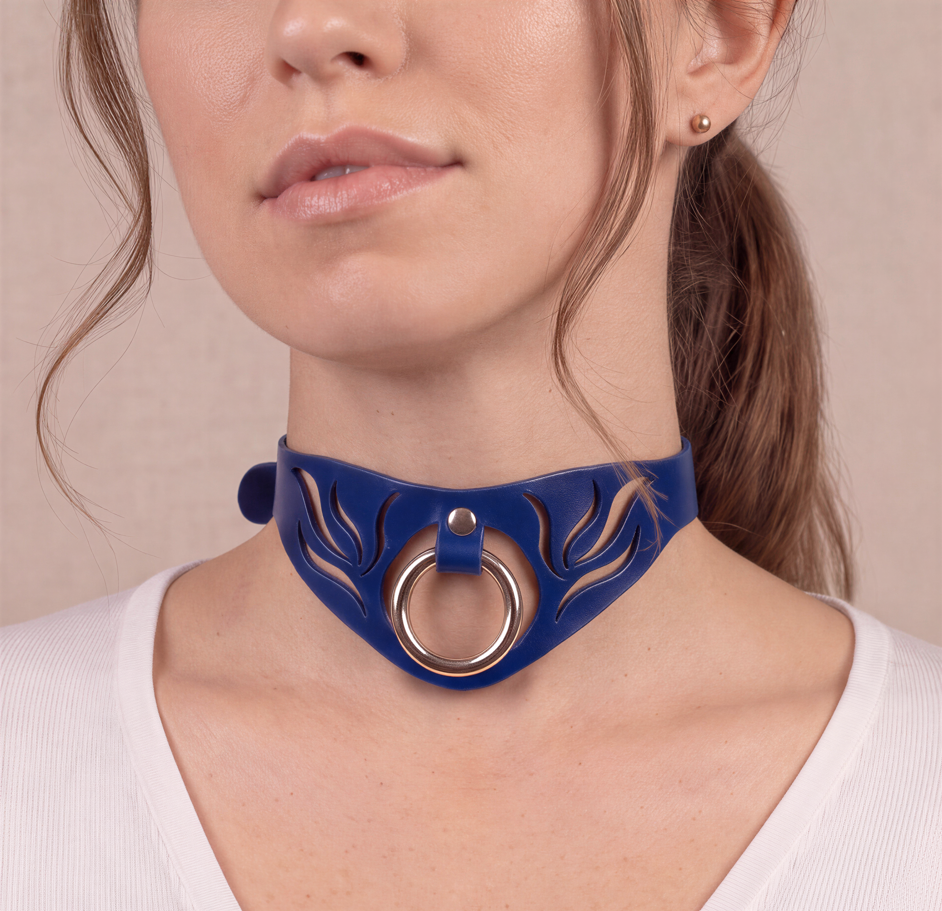 A close-up of a woman's face wearing a blue choker necklace with a silver ring.