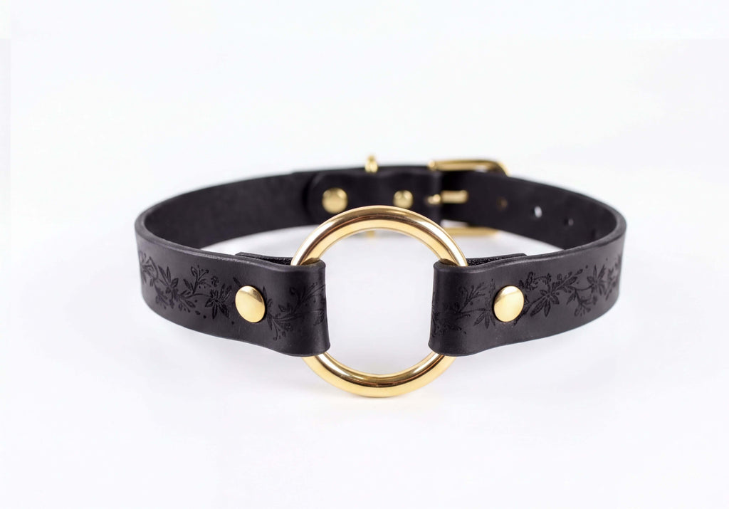 A black leather choker collar with a gold-colored circular buckle.