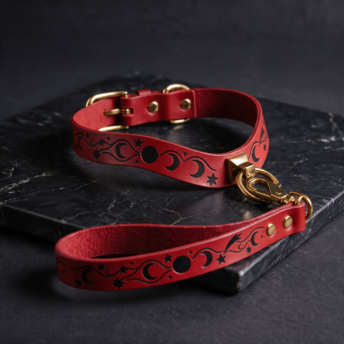 A red leather collar with a metallic buckle and a matching red leather leash with a metallic hook attached, both resting on a black marble surface.