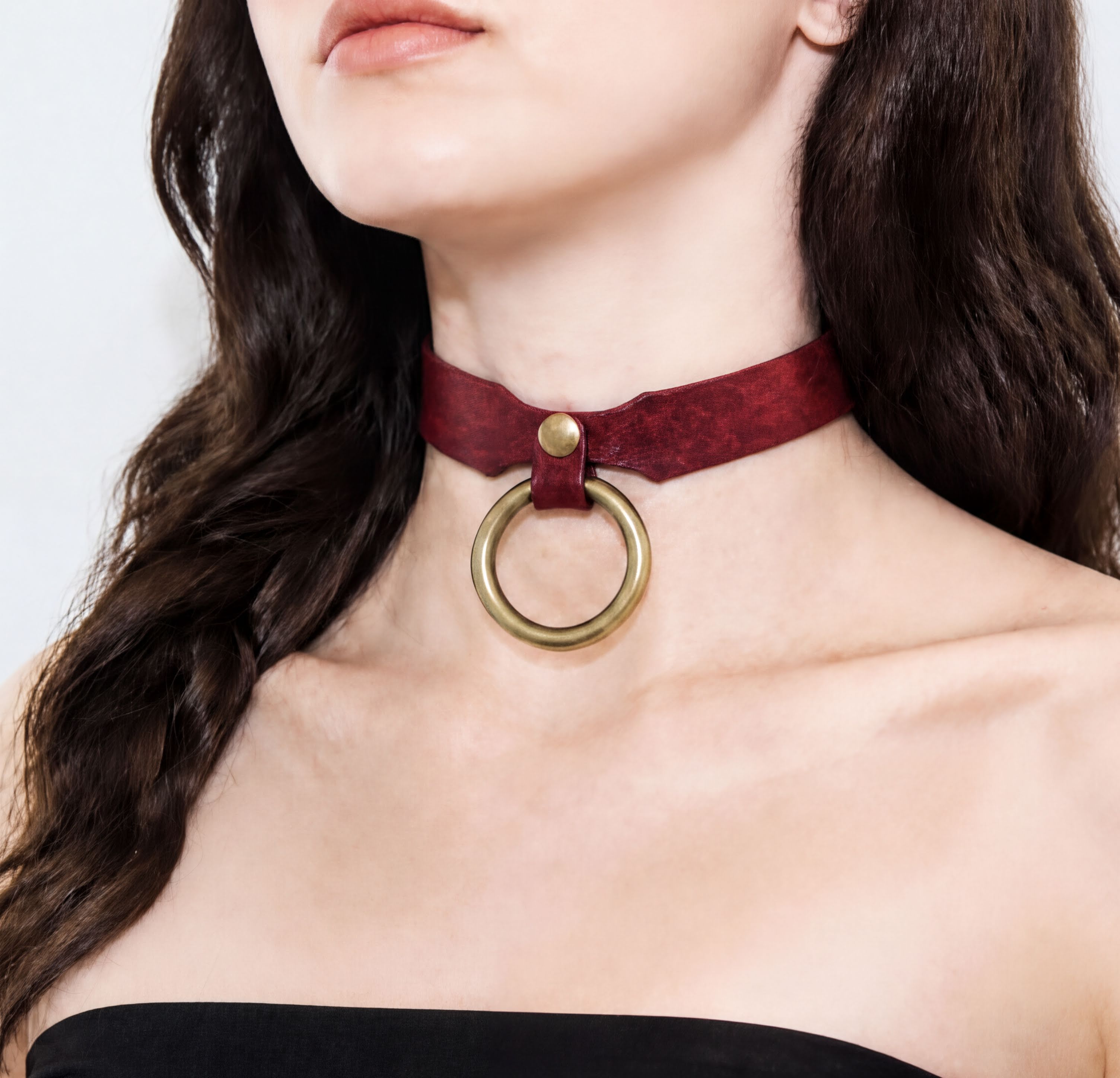A close-up of a woman's neck and chest area wearing a red choker necklace with a gold ring.