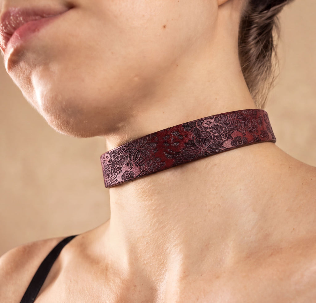 A close-up of a woman's neck and chest area wearing a burgundy choker necklace with a floral pattern.