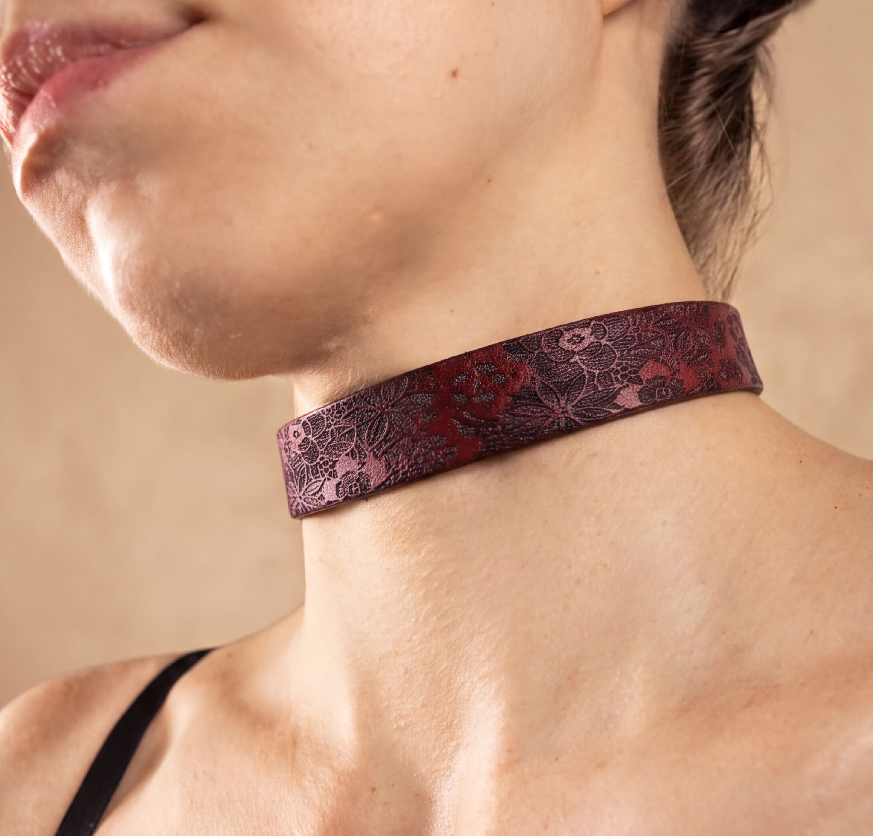 A close-up of a woman's neck and chest area wearing a burgundy choker necklace with a floral pattern.