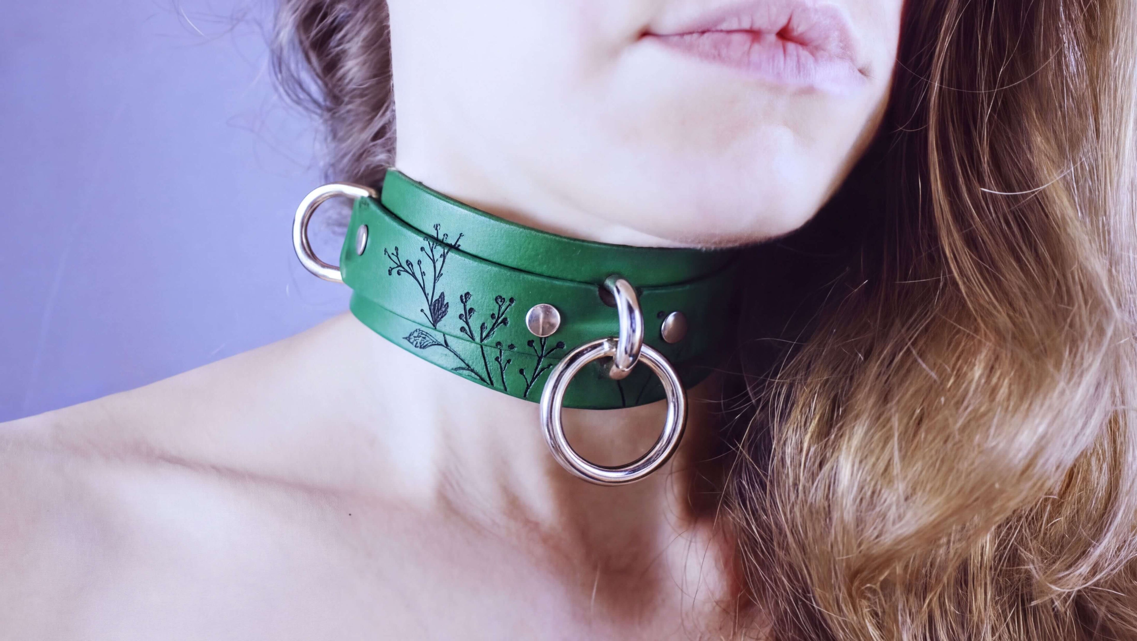 A close-up of a woman's neck and chin wearing a green choker necklace with metal rings and a floral design.