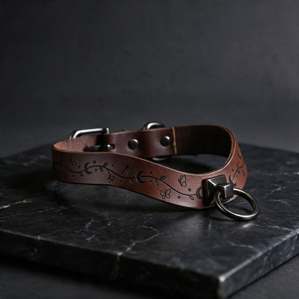 A brown leather collar with a metal ring and decorative elements rests on a dark surface.