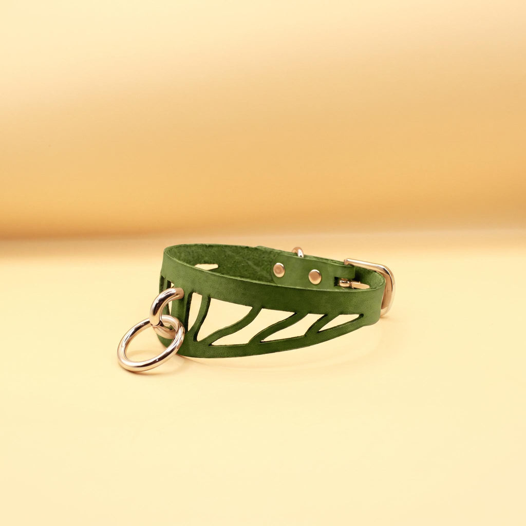 A green leather choker necklace with metal rings and a metal clasp is displayed against a yellow background.
