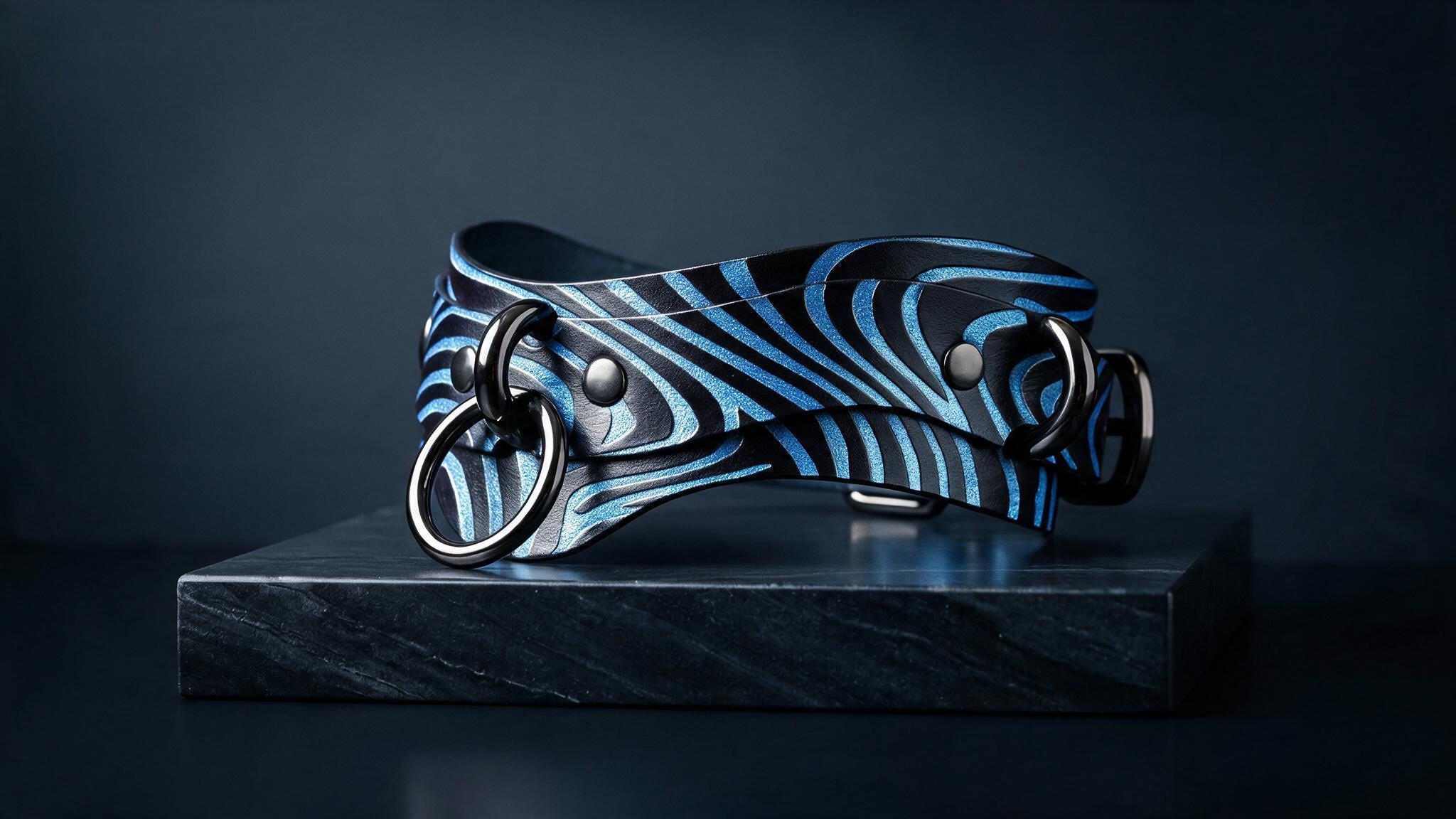 A striking blue and black zebra-striped leather collar with metal rings and buckles is displayed on a black marble pedestal against a dark background.