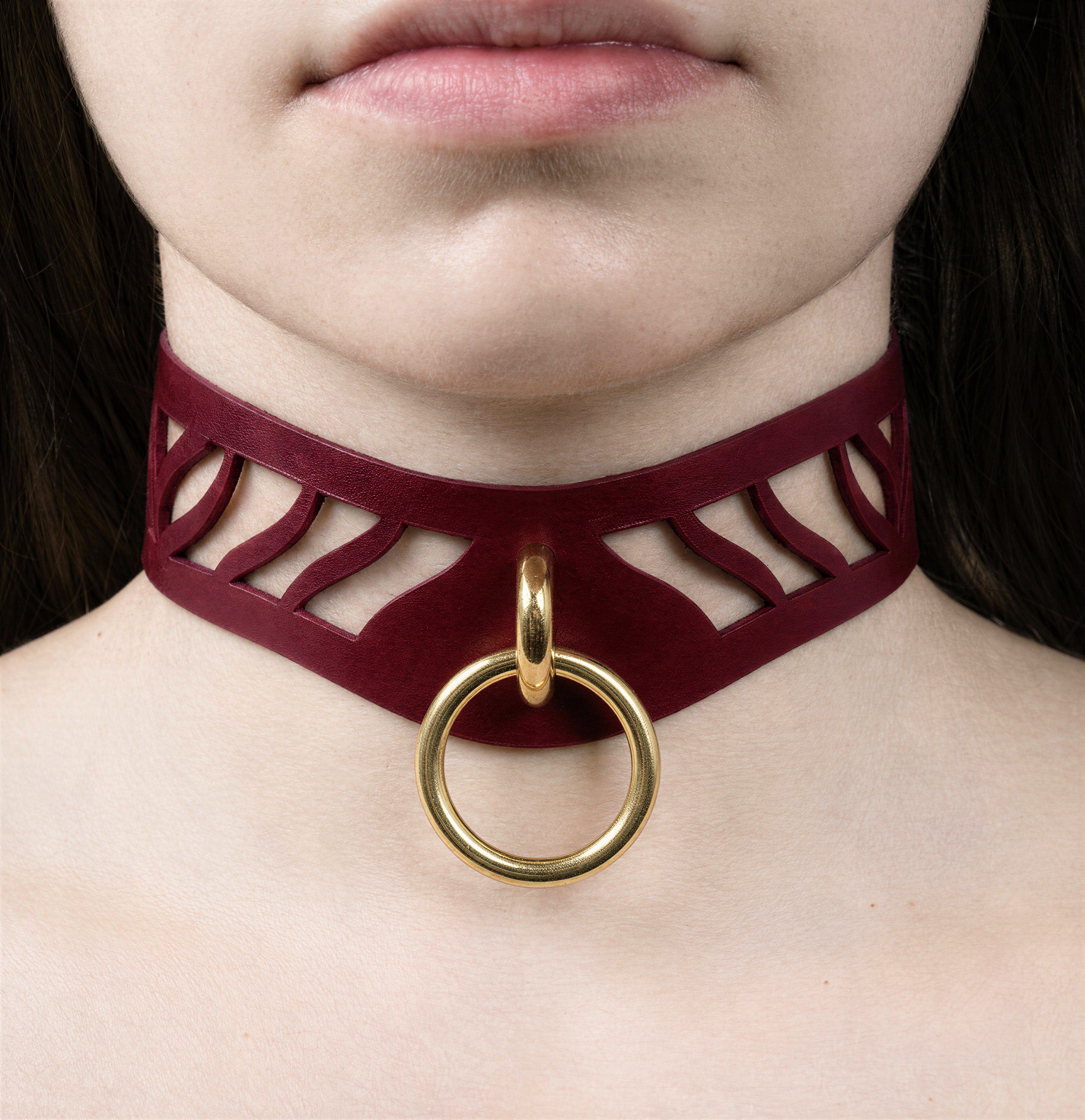 A close-up of a person's neck and chest area wearing a burgundy choker necklace with a gold ring.