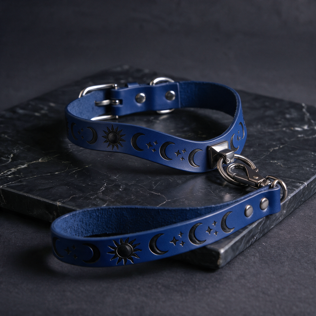 A blue leather collar with moon and star designs, and a matching leash attached to it, resting on a dark surface.