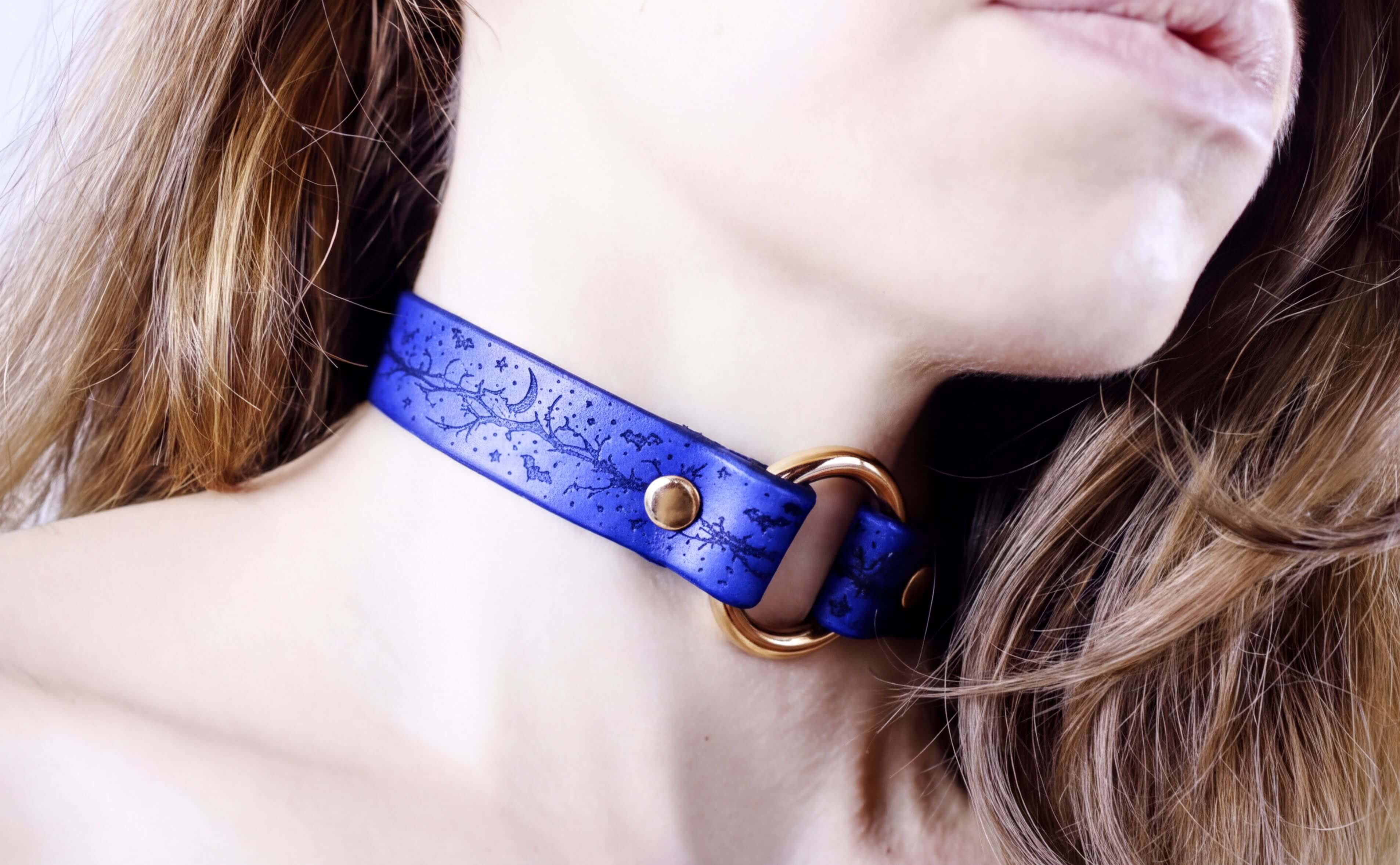 A close-up of a woman's neck wearing a blue choker necklace with a gold-colored buckle.