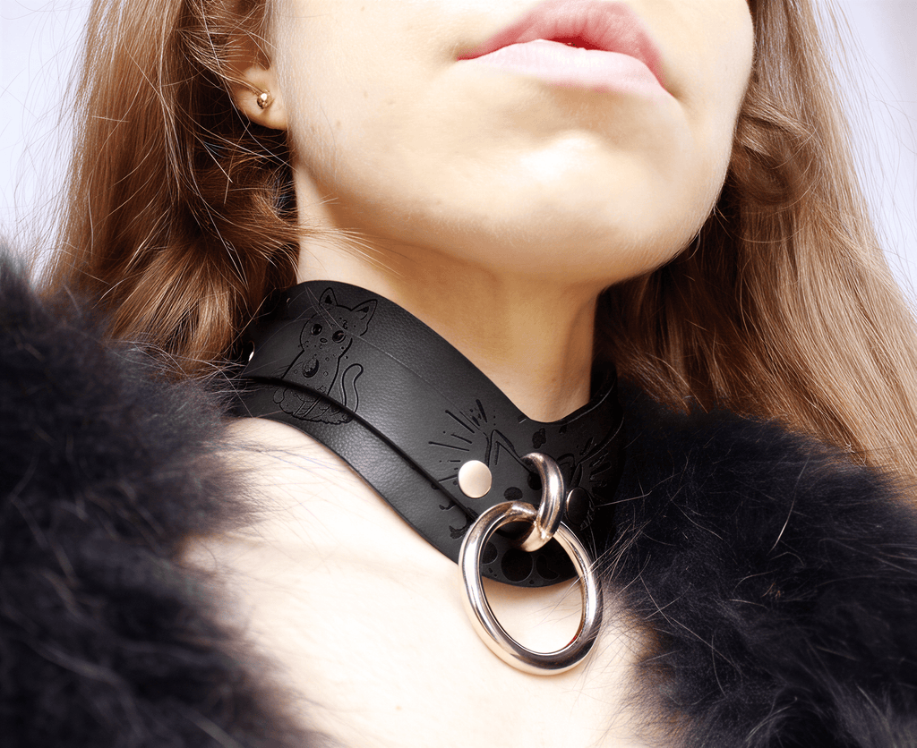 A close-up of a person wearing a black leather choker necklace with a metal ring and a cat design.