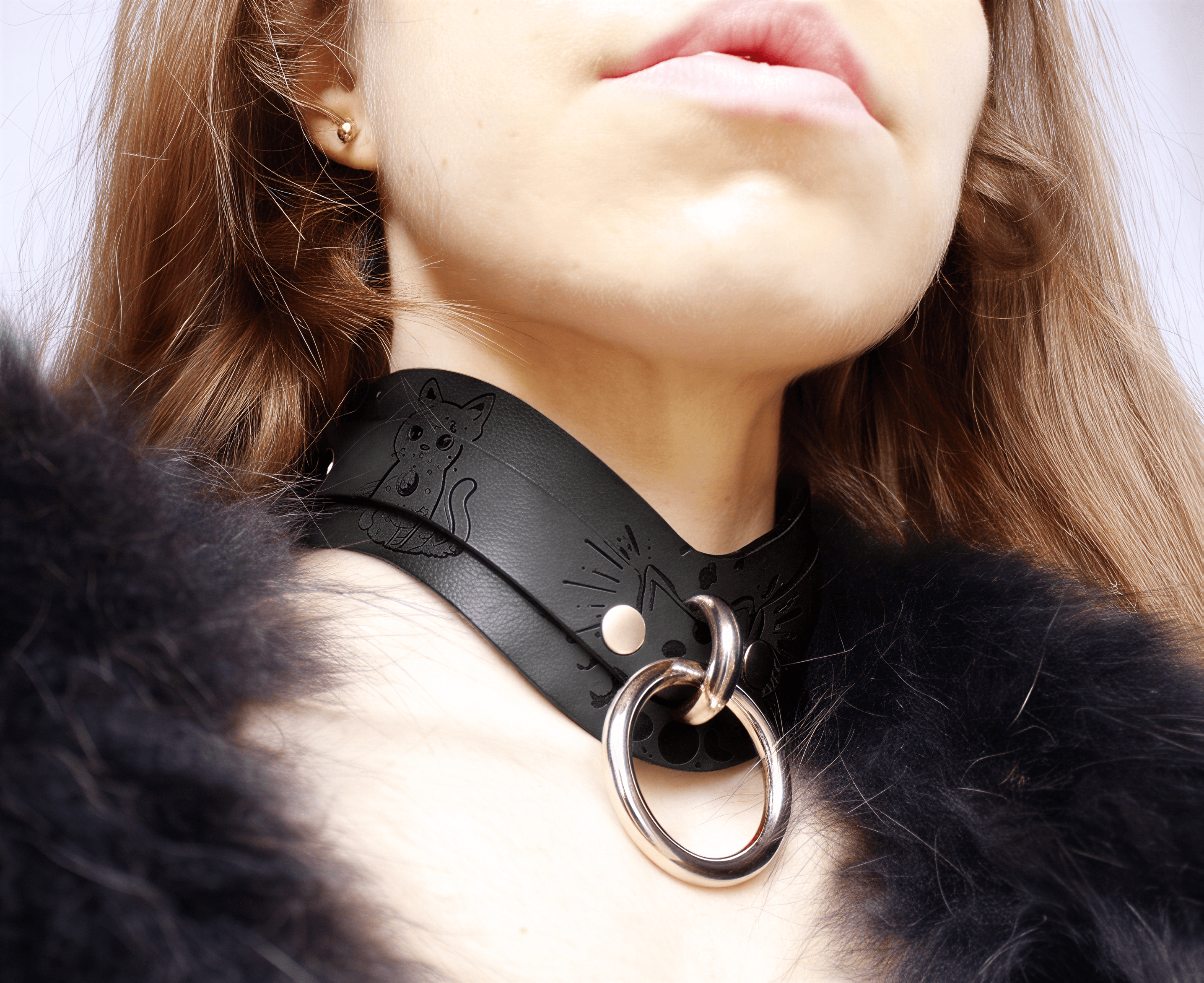 A close-up of a person wearing a black leather choker necklace with a metal ring and a cat design.