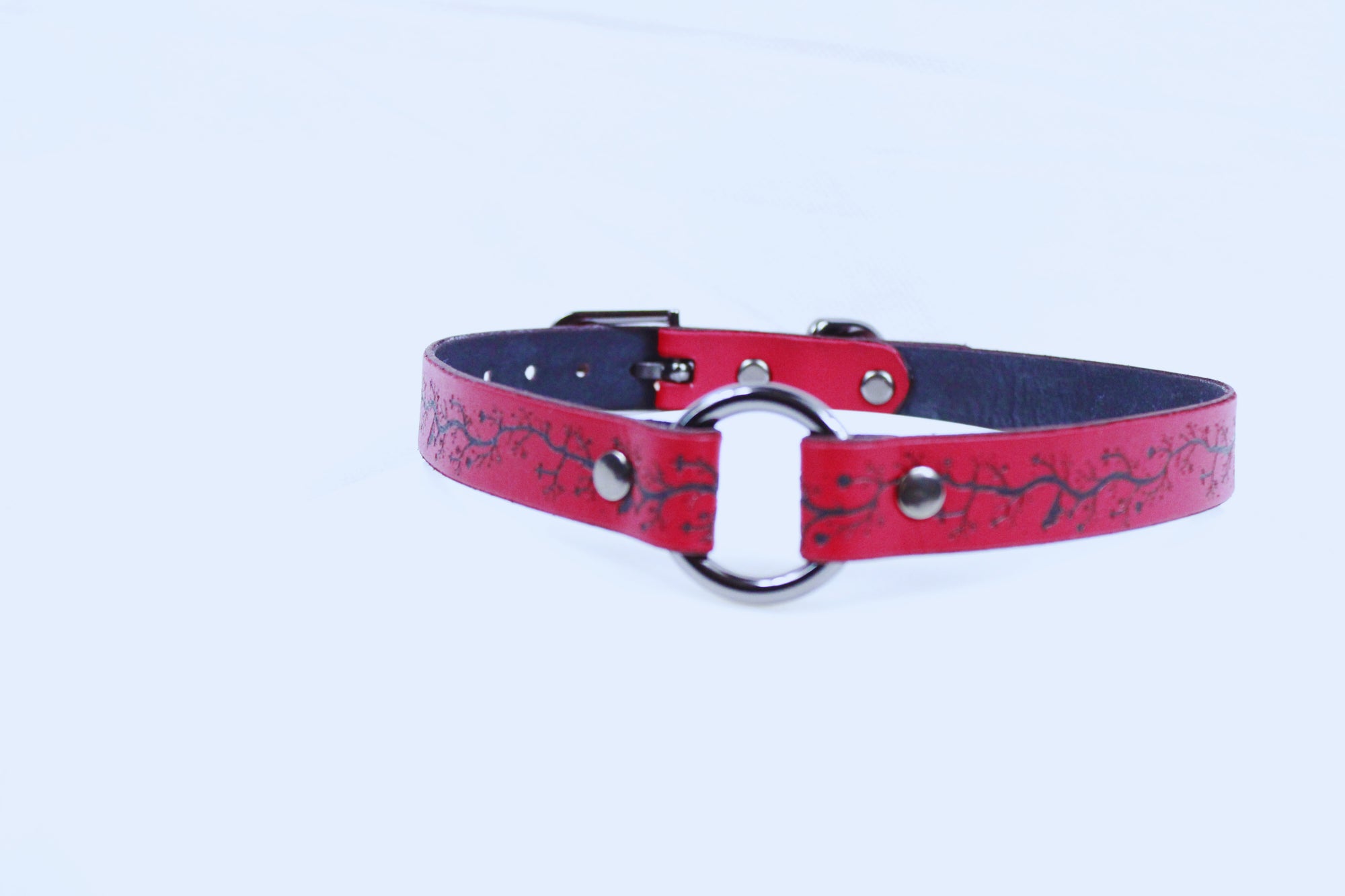 A red leather collar with a black floral pattern and a metal ring on the front.