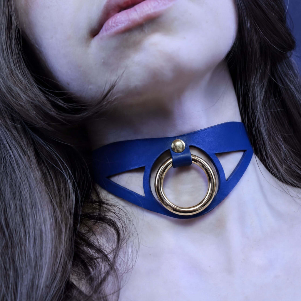 A close-up of a woman's neck and chin wearing a blue choker necklace with a gold ring.
