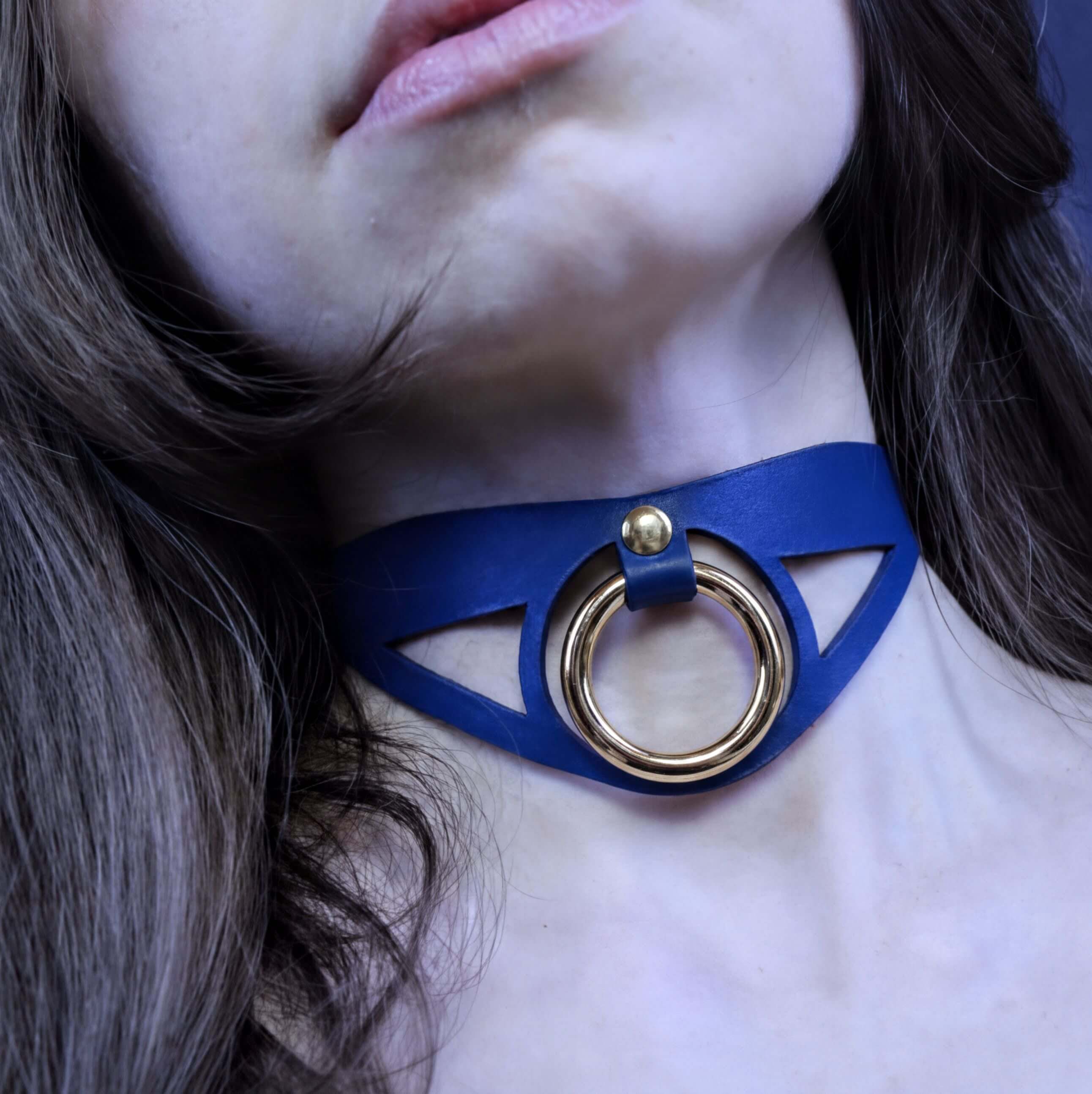 A close-up of a woman's neck and chin wearing a blue choker necklace with a gold ring.