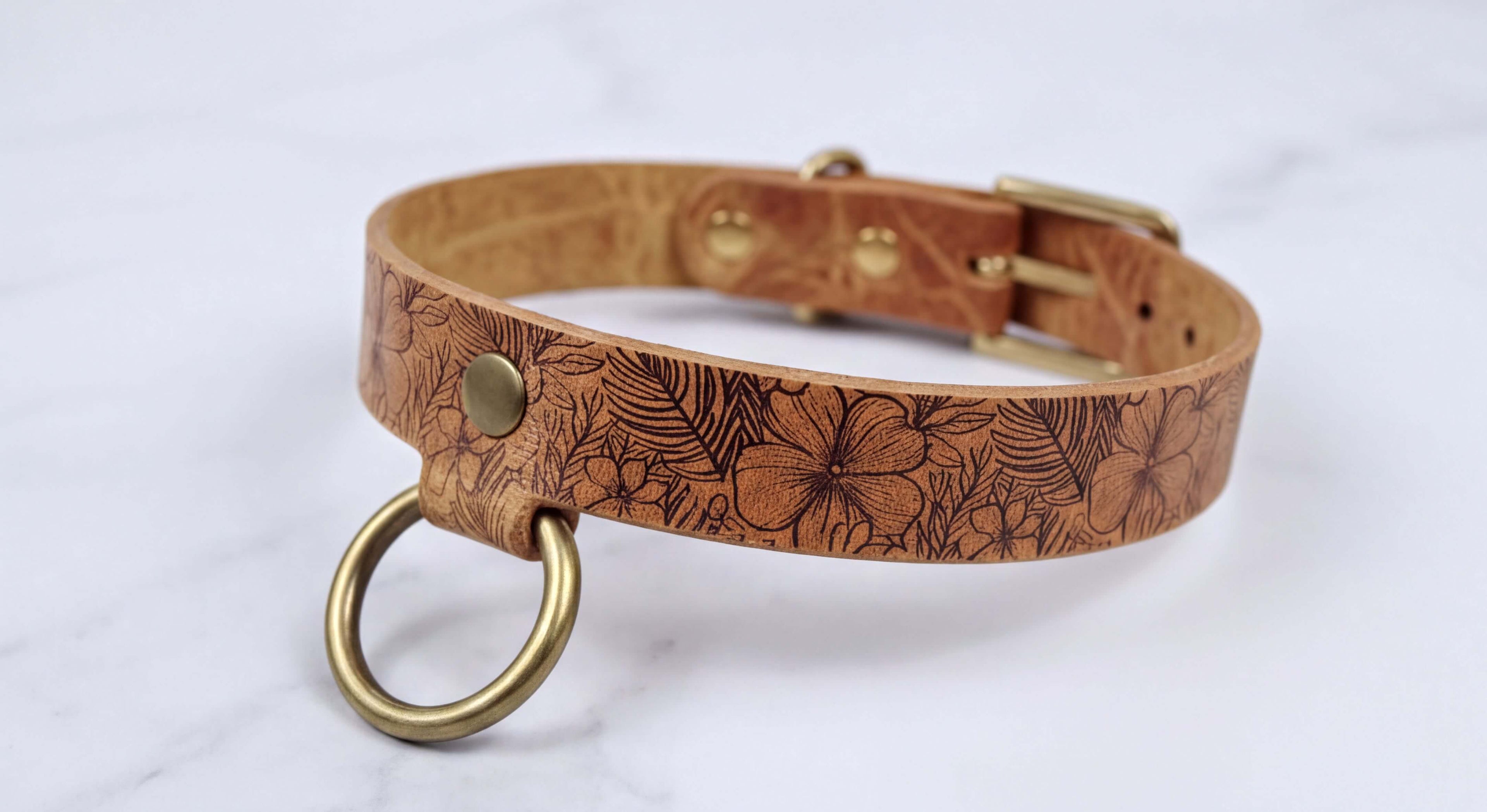 A brown leather collar with a floral pattern and a metal ring attached to it.
