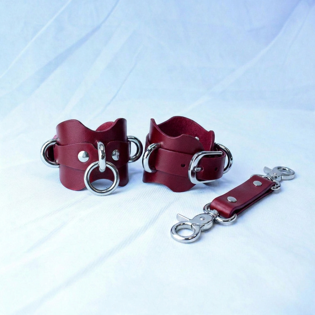 a pair of red leather cuffs with metal rings and buckles, as well as a metal attachment or clasp.