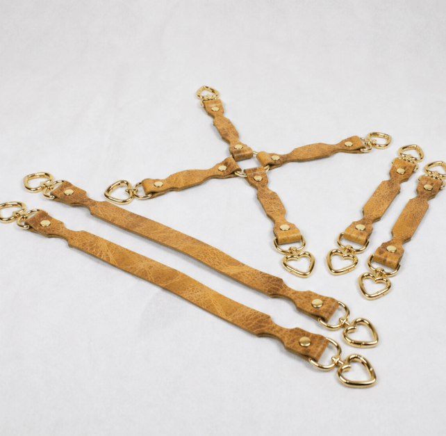 a collection of tan leather straps with gold hardware, including heart-shaped buckles, arranged on a white background.