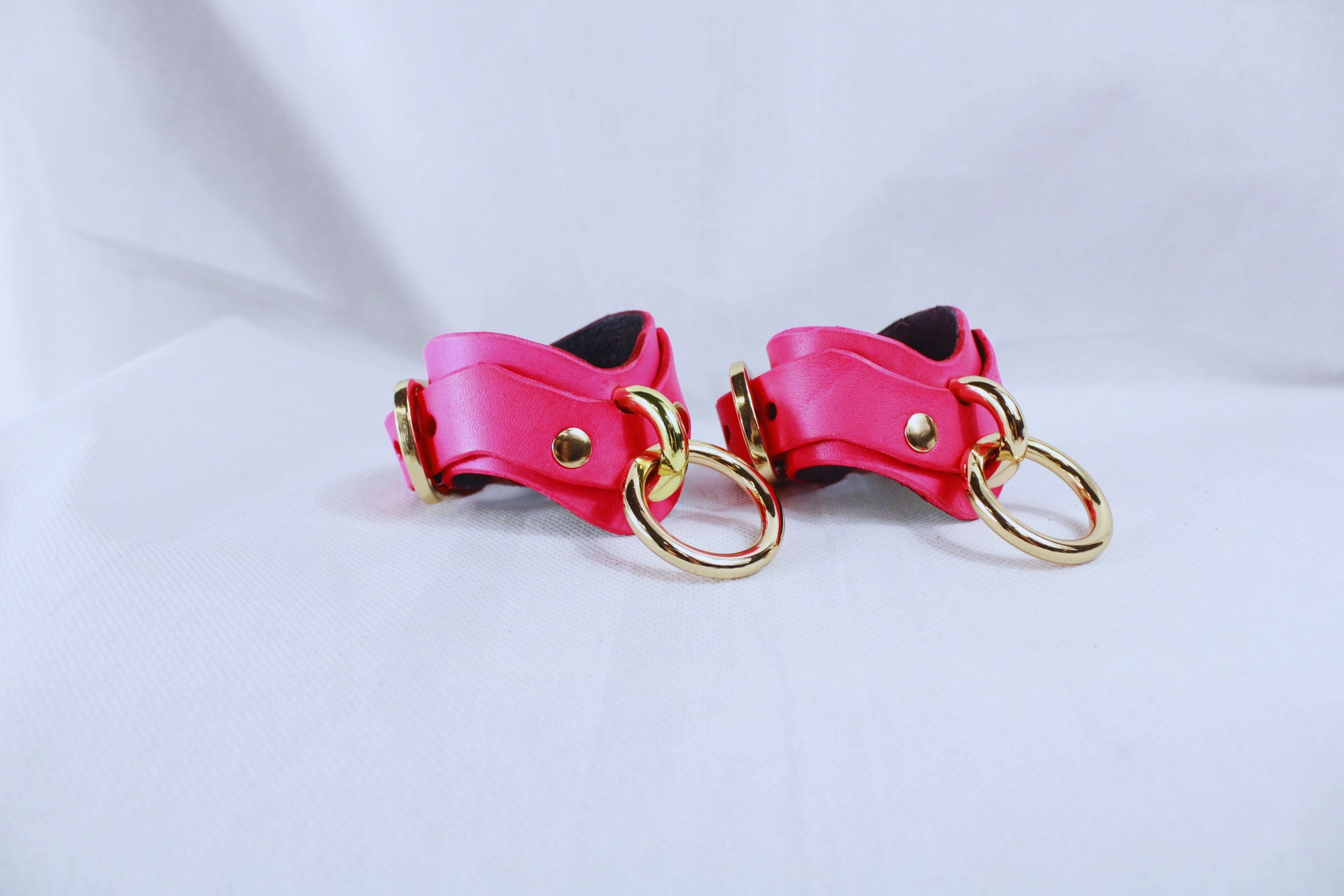 Pink leather cuffs with gold hardware for BDSM, bondage gear, and submissive play. Ideal for comfort and control.