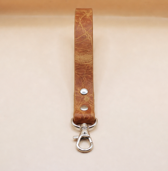A brown leather strap with a metal clasp and hook attached to it.