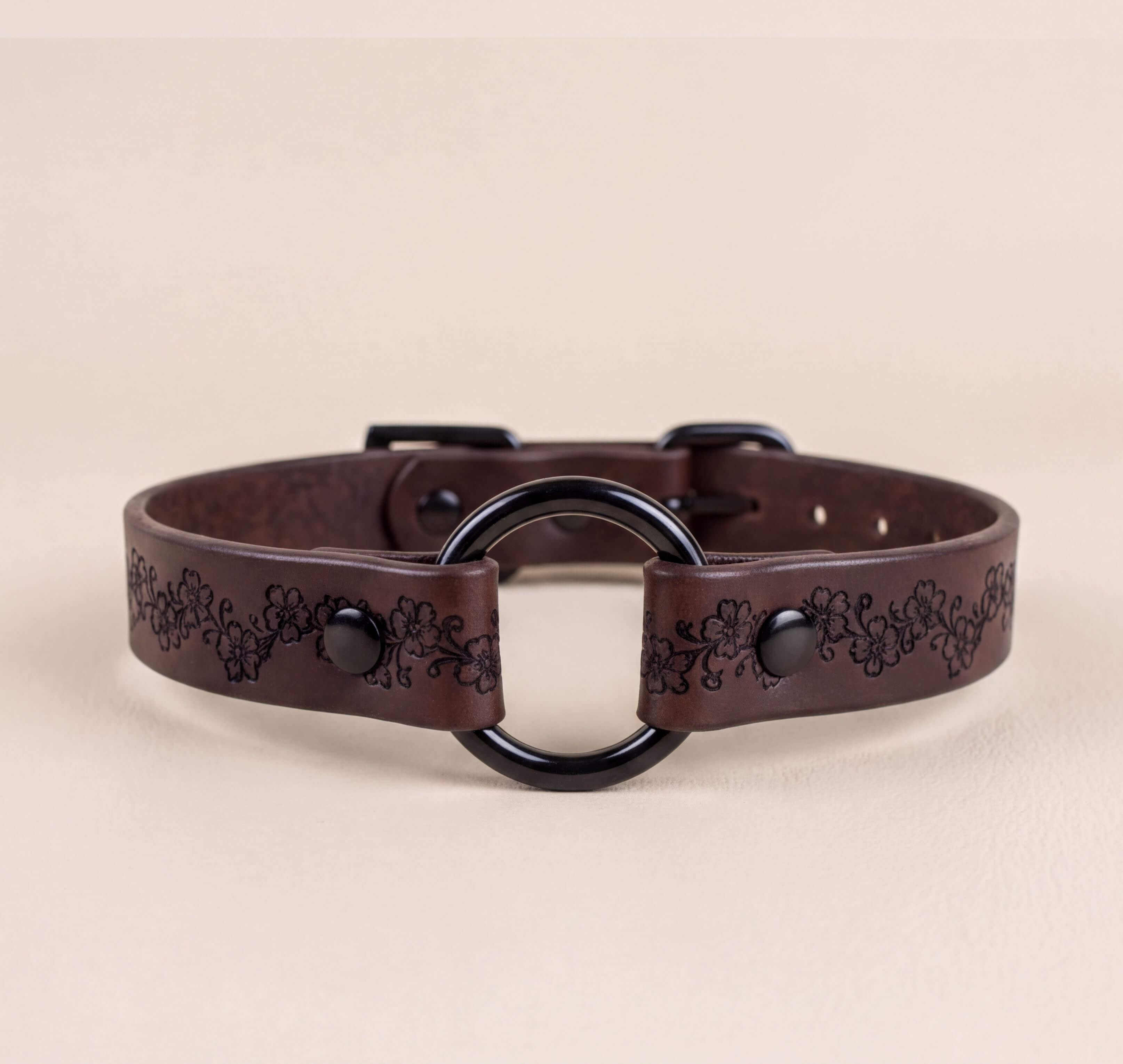 A brown leather collar with a black circular buckle and floral designs on the strap.